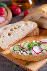 Ciabatta with curd cheese, fresh radish, cucumber on a wooden cutting board - concept of healthy fitness breakfast or snack