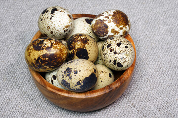 Obraz premium Quail eggs in a round wooden bowl on canvas, close-up, macro. Eggshell stains. Spotted pattern on the eggs. Dietary healthy foods. Egg. 