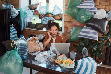 Unkempt young Asian woman having phone conversation at her cluttered flat
