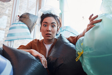Asian female trying to get out of a huge pile of garbage indoors