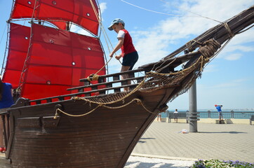 boy looks into the distance on an old ship with red sails. boy under the red sail