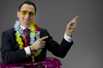 Caucasian handsome businessman in yellow sunglasses, strict suit with lei over neck and rubber ring...