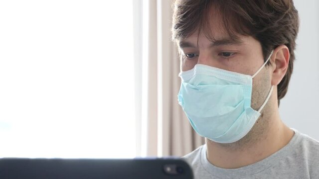 Man working in bed, with a facemark, doing home office because he is sick. In 4k