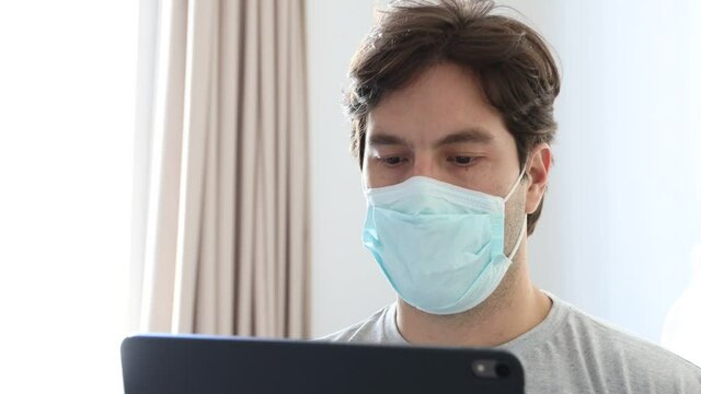 Man working in bed, with a facemark, doing home office because he is sick. In 4k
