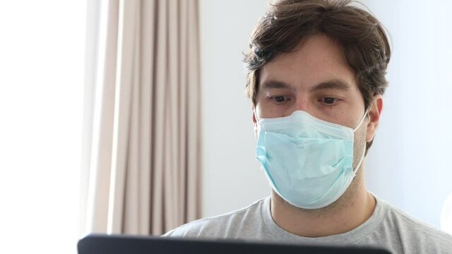 Man working in bed, with a facemark, doing home office because he is sick. In 4K