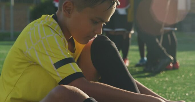 Mixed race soccer kid lacing up his shoe in a sunny day