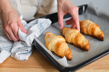Obraz na płótnie Canvas A woman is cooking croissants. Finished baking. Delicious traditional french crispy croissants for breakfast. Homemade bakery, cuisine for family. Girl chef work on kitchen table. Raw croissants