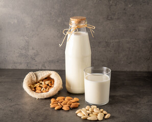 against a dark background almonds in different forms, milk in a bottle and next to a glass with almond milk