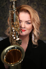 Portrait of a charming blonde with a saxophone in her hands. Beautiful girl in a black evening...