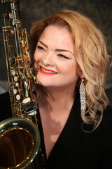 Portrait of a charming blonde with a saxophone in her hands. Beautiful girl in a black evening...