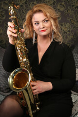 Portrait of a charming blonde with a saxophone in her hands. Beautiful girl in a black evening...