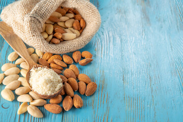 mixed almonds in a bag on a blue wooden table. on a wooden spoon - a handful of almond flour, and around - peeled and unpeeled almonds