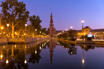 North Tower and Canal - A wide-angle dawn view of the north tower of Plaza de España, reflected in the calm water of the canal, on a clear Autumn morning. Seville, Andalusia, Spain. - obrazy, fototapety, plakaty