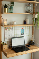 Small home office remote station, with laptop, houseplants, metallic board, candles and table lamp. Vertical shot.