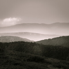 B&W fine art composition of multiple layers of sunlit mountains with mist between them and a hazy sky