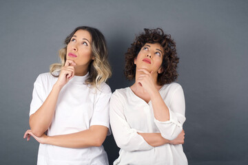 Portrait of thoughtful smiling girl keeps hand under chin, looks sideways, thinking or wondering about something with interest, dressed casually, poses against gray studio. Taking decisions concept.