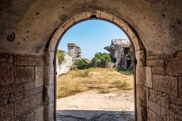 Naklejka premium Ruins of Austro-Hungarian Fortification Fort Forno in Istra, Croatia. Looking out from arched stone passage hallway. Abandoned landmark dating back to 1904 covered with vegetation in bad shape
