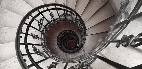 A spiral staircase spiraling down about five floors. The winding concrete stairs are empty. The...