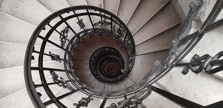 A spiral staircase spiraling down about five floors. The winding concrete stairs are empty. The metal hand rail is nicely decorated. The image approaches the golden ratio and Fibonacci spiral.