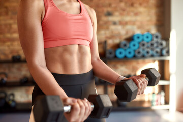Cropped shot of athletic woman showing muscle while working out using dumbbells in gym. Sport,...