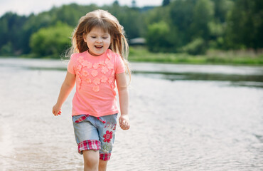 Cute happy little girl running along the beach in shorts and a pink tank top. Beautiful summer...