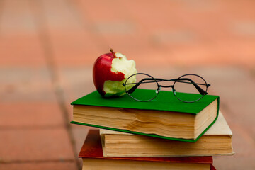 on the sidewalk near the school are school books, glasses and a red Apple