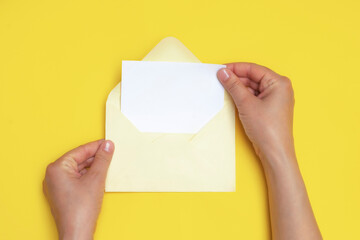 Woman hands holding an open envelope with blank white card on yellow background, mockup