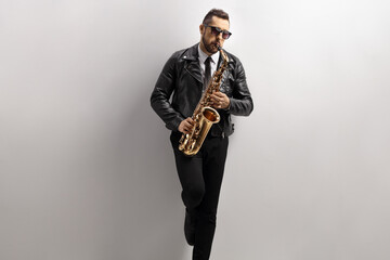 Man playing a saxophone and leaning on a gray wall