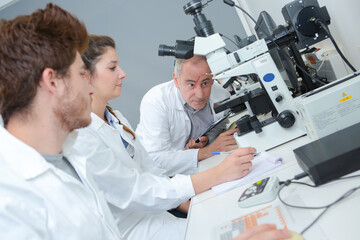 Naklejka na ściany i meble Group of students with microscope in laboratory