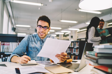 Smiling male student making coursework project in college library