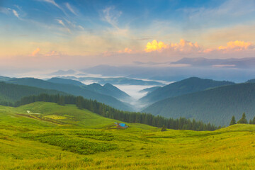 Magic dawn on a pasture in the mountains. 
Shepherd's house in the meadow. 
The fog spreads in the valley. 
Beautiful clouds in the blue sky.  Ukraine, Europe.