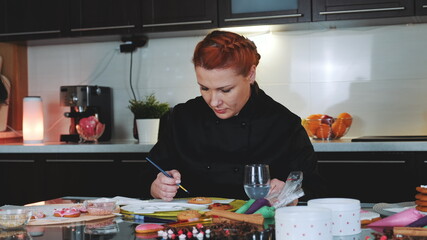 Bakery worker providing masterclass of cookies decoration. She painting cookies with special brush and food colors.