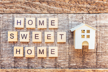 Miniature toy house with inscription HOME SWEET HOME letters word on wooden background. Mortgage property insurance dream home concept. Flat lay top view copy space