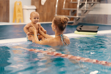 Young mother and her baby enjoying a baby swimming lesson in the pool. Child having fun in water with mom