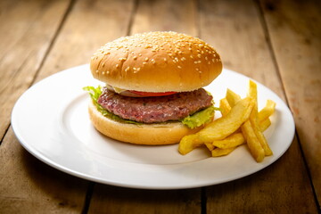 Burger with potatoes on white plate on wooden table