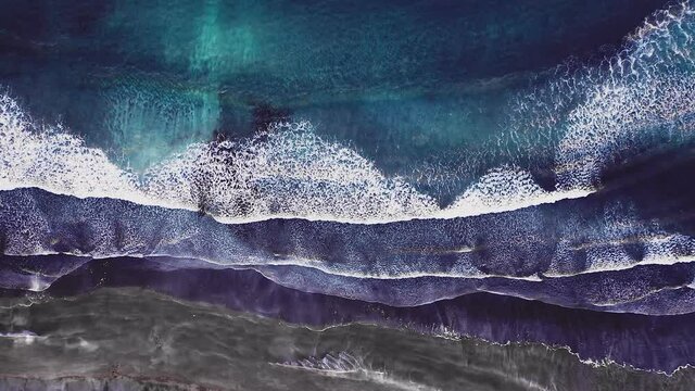 Aerial view of beautiful beach with view of ocean waves and water crashing on to sandy shore from top angle. Faroe Islands beach with waves crashing to shore. No people, epic dramatic wild beach
