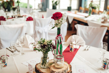 Close up of red rose flower in decorated high glass vase and arrangement of glassware. Festive table decoration. Celebration, wedding, birthday
