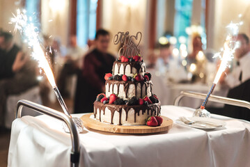 Three-tiered wedding cake with dripped chocolate and berries standing on serving table. Mr. and...