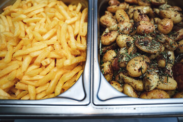 Two potato side dishes in separate hotel pans. French fries and baked potatoes at self-service buffet table. Celebration, party, birthday or wedding