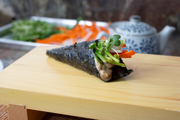 A closeup view of a hand roll, also known as temaki, in a restaurant or kitchen setting.