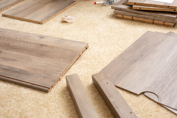 A view of several wood board pieces spread across the carpet during a session of living room furniture assembly.