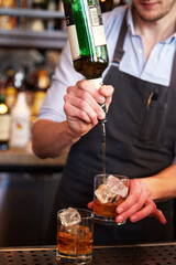 A bartender pouring whiskey into a glass to prepare for mixing a cocktail.