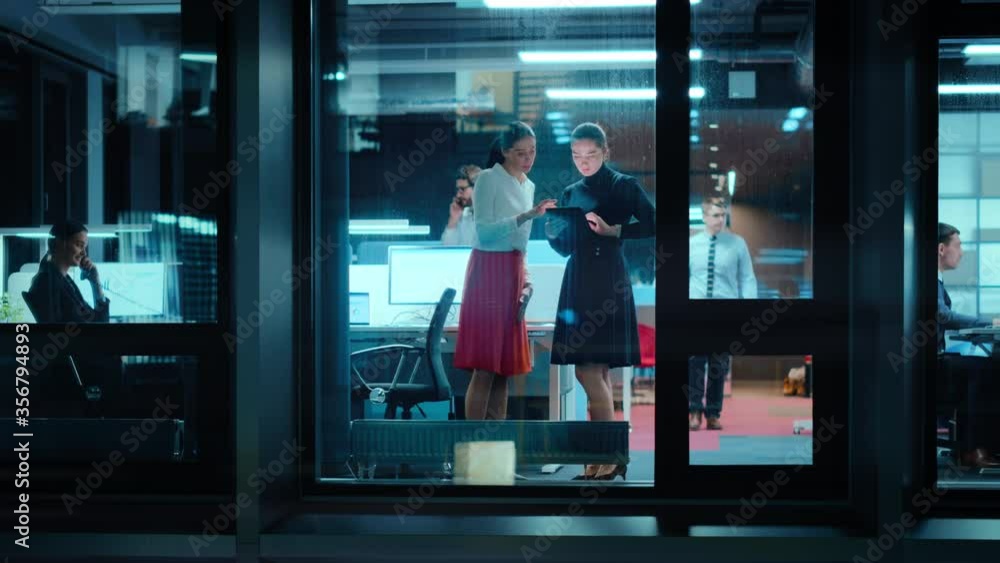Poster footage from outside: two businesswomen working on a tablet computer in office. managers standing by