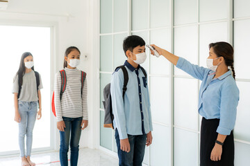Asian woman teacher using thermometer temperature screening student for fever against the spread of COVID-19 while student coming back to school, New normal and Education concept.