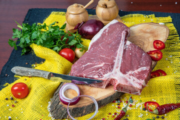 Raw T-bone Steak for grill or BBQ on cutting board over,  yellow linen background, top view.