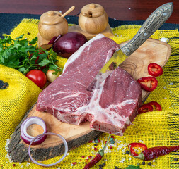 Raw T-bone Steak for grill or BBQ on cutting board over,  yellow linen background, top view.