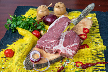 Raw T-bone Steak for grill or BBQ on cutting board over,  yellow linen background, top view.
