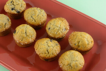 Closeup of mini bite-size blueberry muffins on red brunch plate on green background