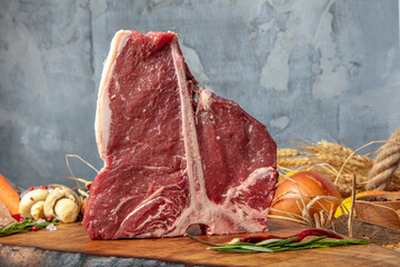 Raw t bone steak is on a wooden Board on black background, next to salt, pepper and herbs.
