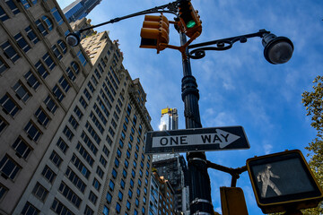 A one way street sign in New York. A crosswalk street sign. Busy city. Metal lamp post and traffic...